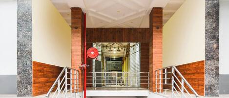 A staircase leading to a covered entrance with a metal railing and a red fire alarm.