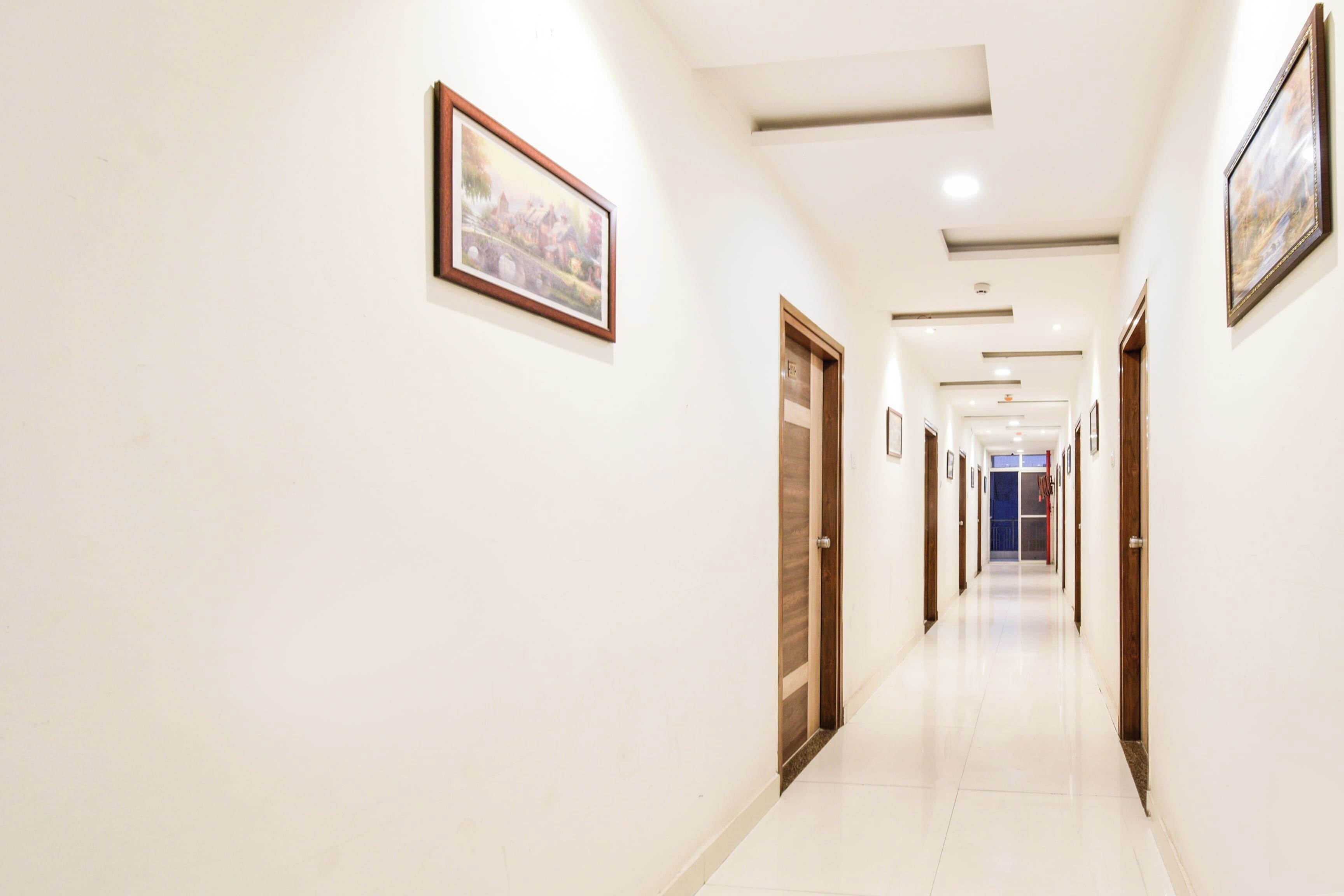 Un pasillo de hotel con puertas a ambos lados, suelo de baldosas y cuadros en las paredes.