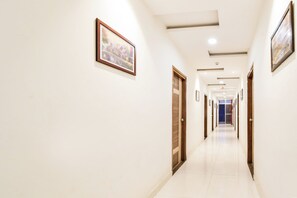 A hotel corridor with doors on both sides, a tiled floor, and framed pictures on the walls.