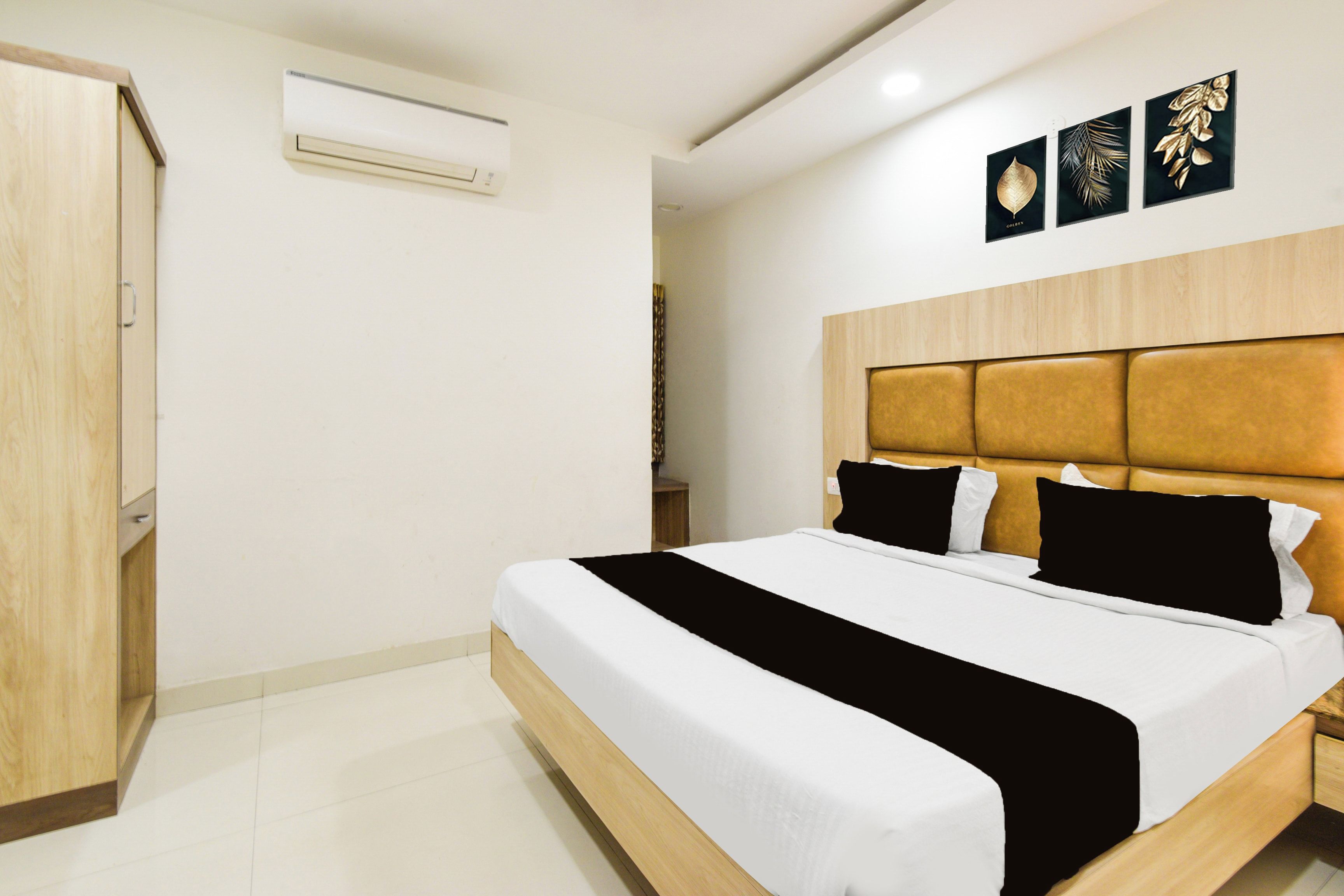 Una habitación de hotel con una cama, un armario, un aire acondicionado de pared y tres cuadros enmarcados.