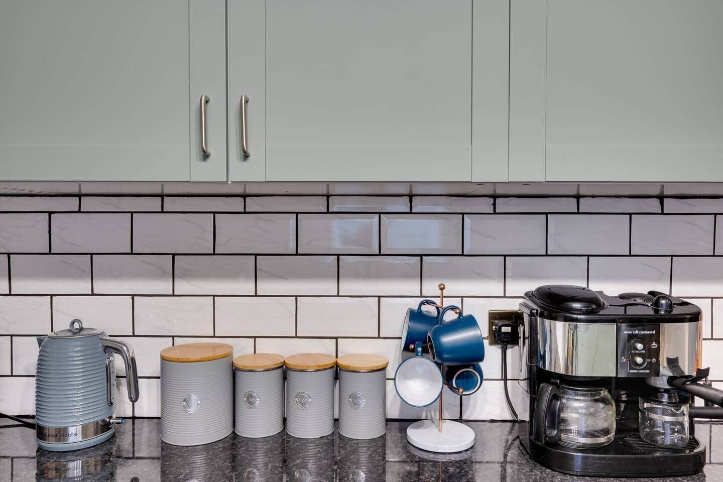 Een keuken met een koffiezetapparaat, een waterkoker en diverse opbergcontainers.