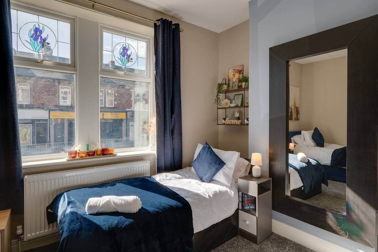 Ein Hotelzimmer mit Bett, Nachttisch, Spiegel, Fenster mit Vorhängen und Blick auf die Straße.