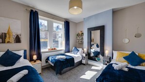 Quarto de hotel com duas camas, uma janela grande com cortinas, um espelho e uma pintura da paisagem urbana.