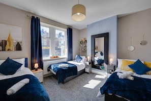 Habitación de hotel con dos camas, un ventanal con cortinas, un espejo y un cuadro de paisaje urbano.