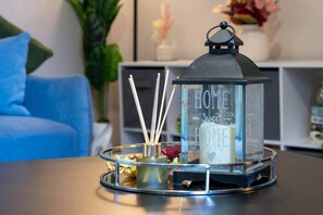 Una linterna de vidrio con la leyenda 'HOME Sweet HOME', sobre una mesa con un sofá azul y una planta al fondo.