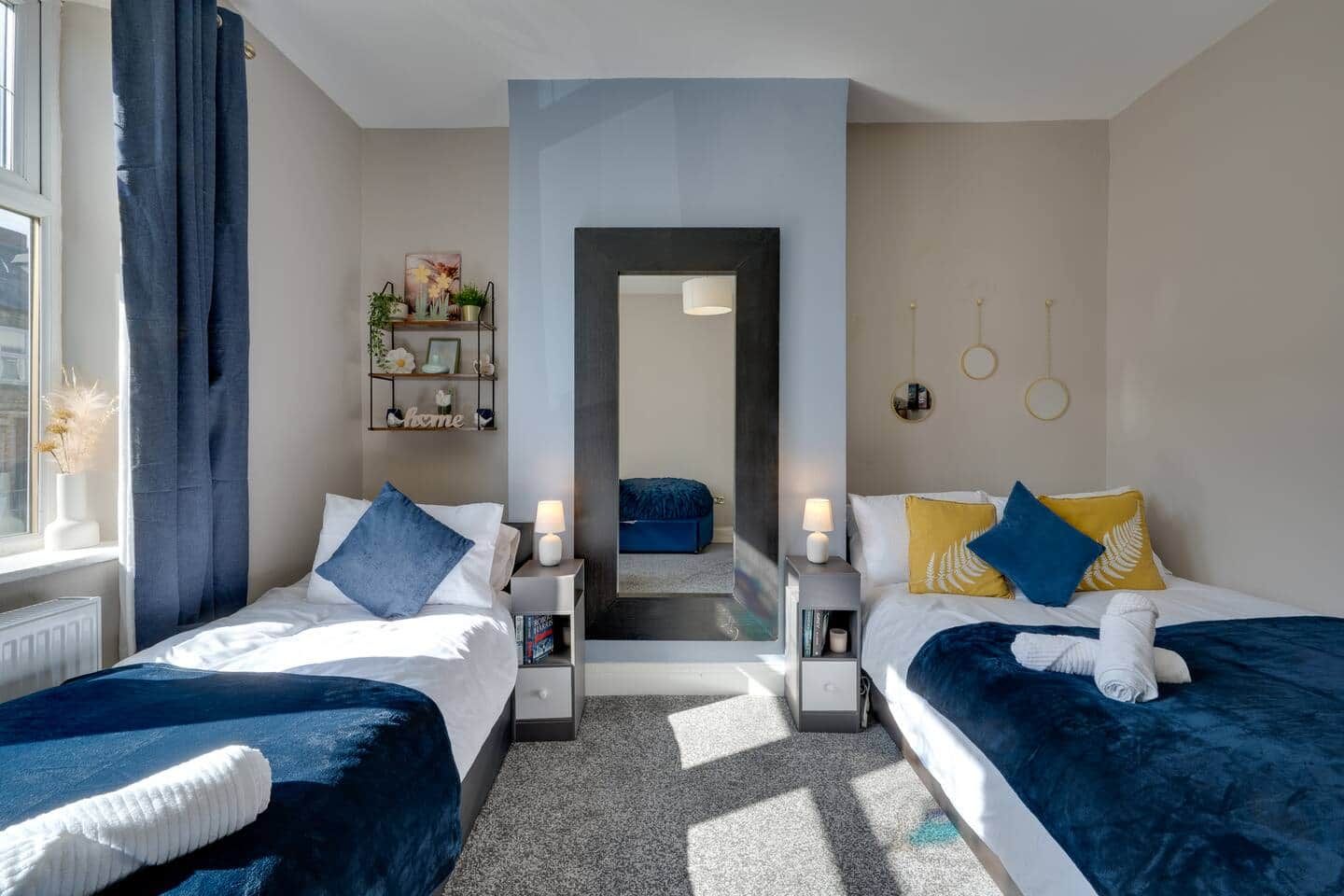Een hotelkamer met twee bedden, een spiegel, een plank met decoratieve objecten en uitzicht op de gang.