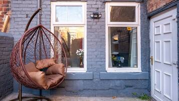 A hanging chair in a courtyard with a brick wall, two windows, and a door.
