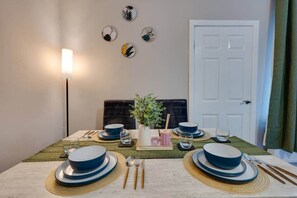 Una mesa de comedor dispuesta con platos, fuentes y cubiertos azules y blancos, un posavasos verde y una pequeña maceta.