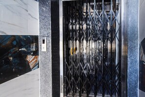 A black metal elevator door with a diamond-patterned grille. - Super Townhouse Hitech City (Hyderabad)