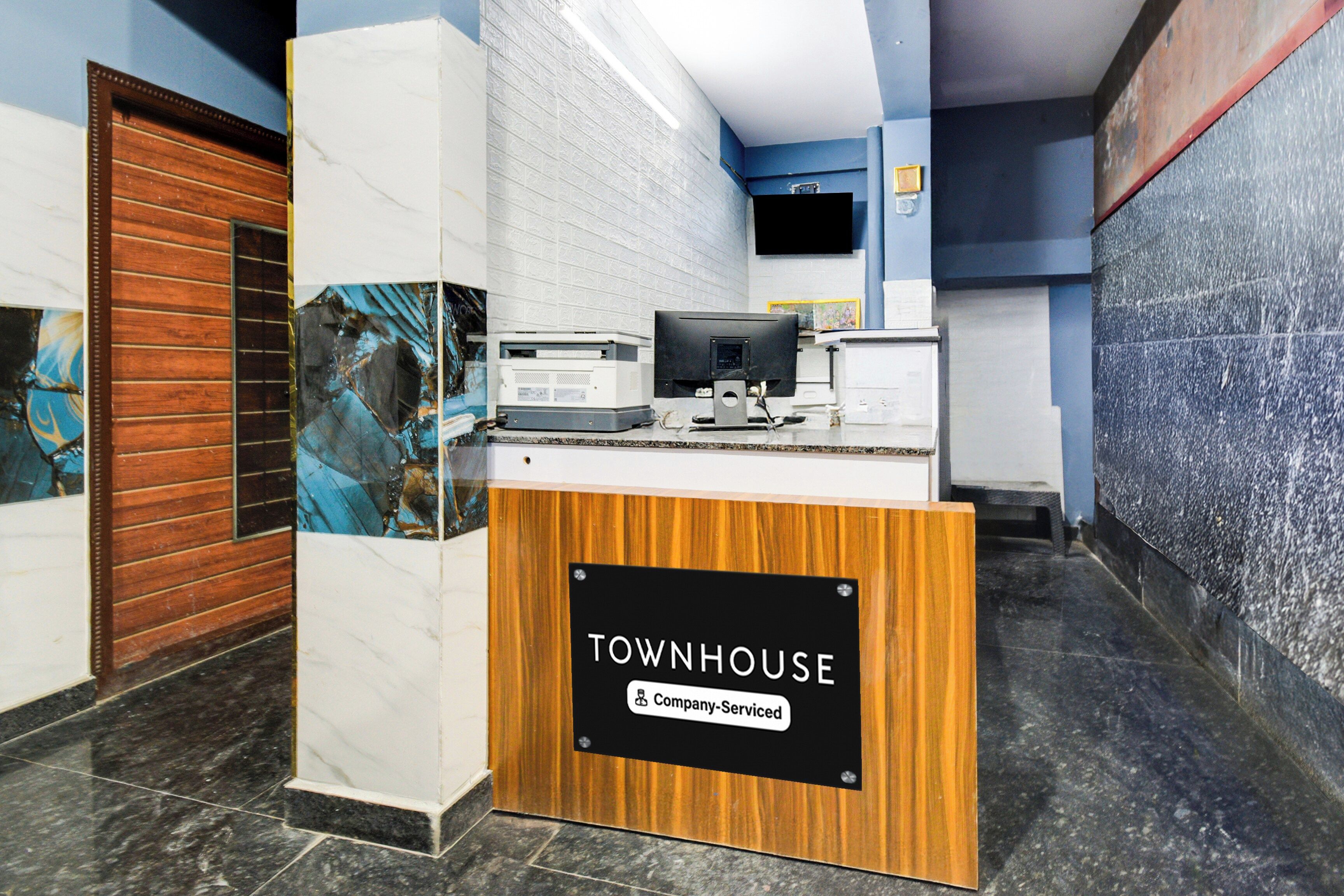 Una taquilla de recepció amb un cartell que diu 'TOWNHOUSE Company-Serviced' a un vestíbul modern amb paviment de marbre i una porta de fusta.