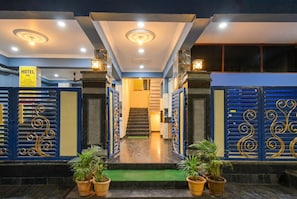Entrada de un hotel con una escalera que lleva al piso superior, una recepción y un letrero con el nombre del hotel.
