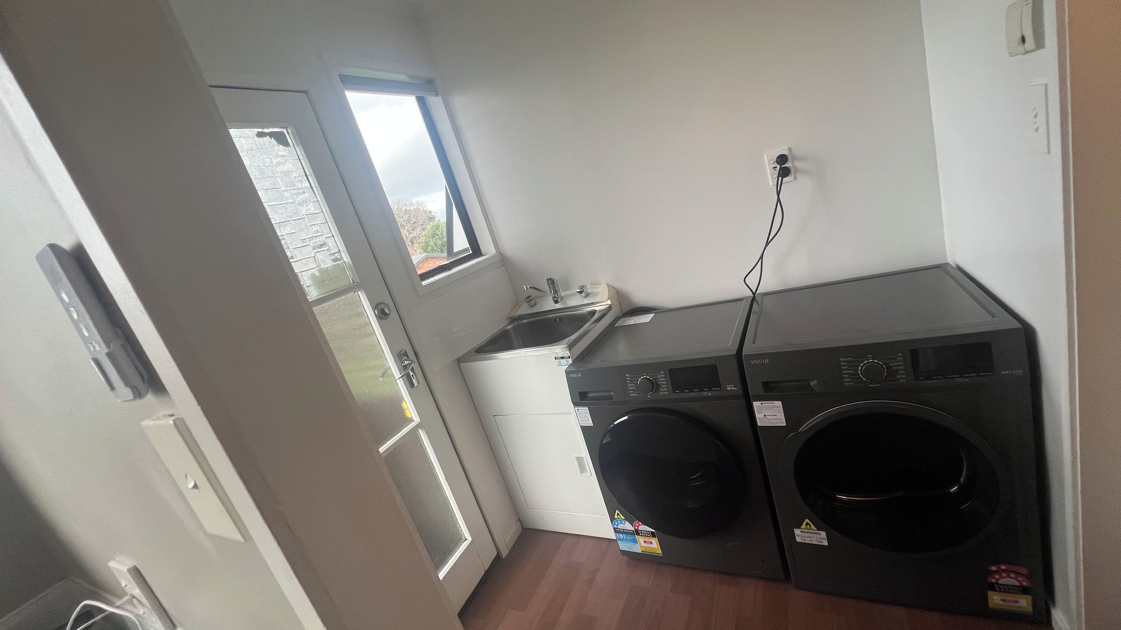A compact laundry room with a front-loading washer and dryer, a small sink, and a window providing natural light.