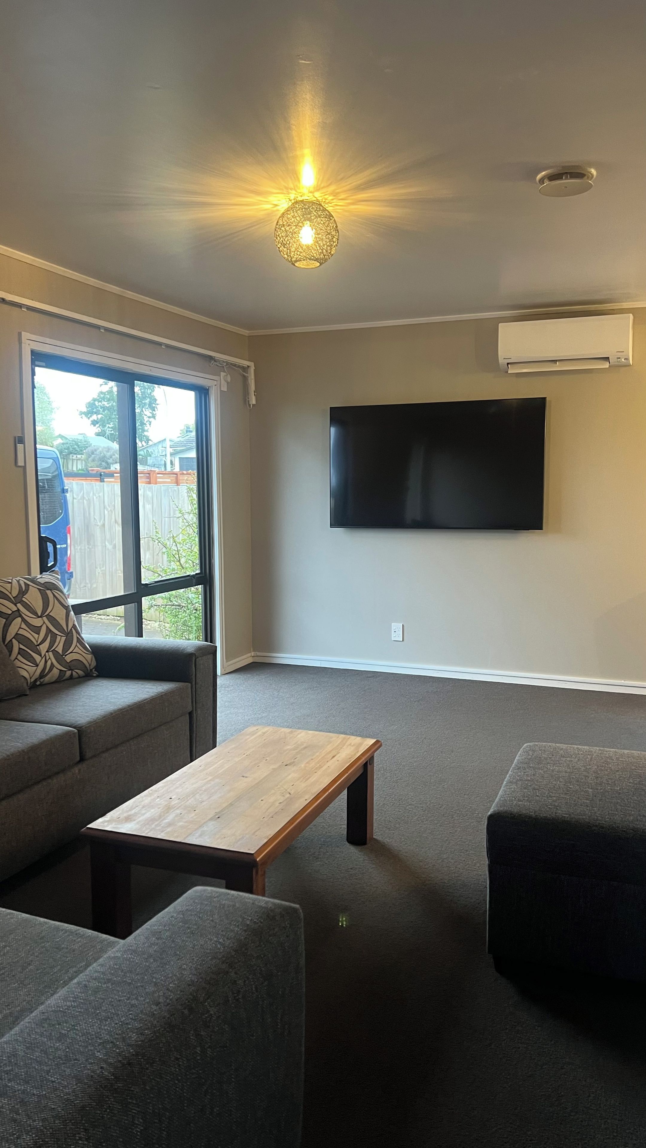 A living room with a sofa, a coffee table, and a TV mounted on the wall.