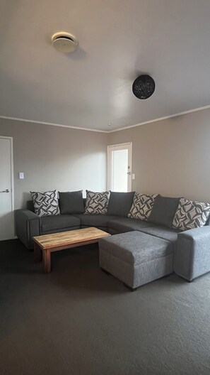 A modern living room with a sectional sofa, a wooden coffee table, and a ceiling light fixture. - Pukekohe 3 Palms 45 Hooper Ave (Pukekohe)