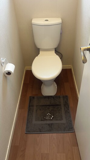 A toilet with a white seat and tank, a black mat with a logo in the center, and a wooden floor. - Pukekohe 3 Palms 45 Hooper Ave (Pukekohe)