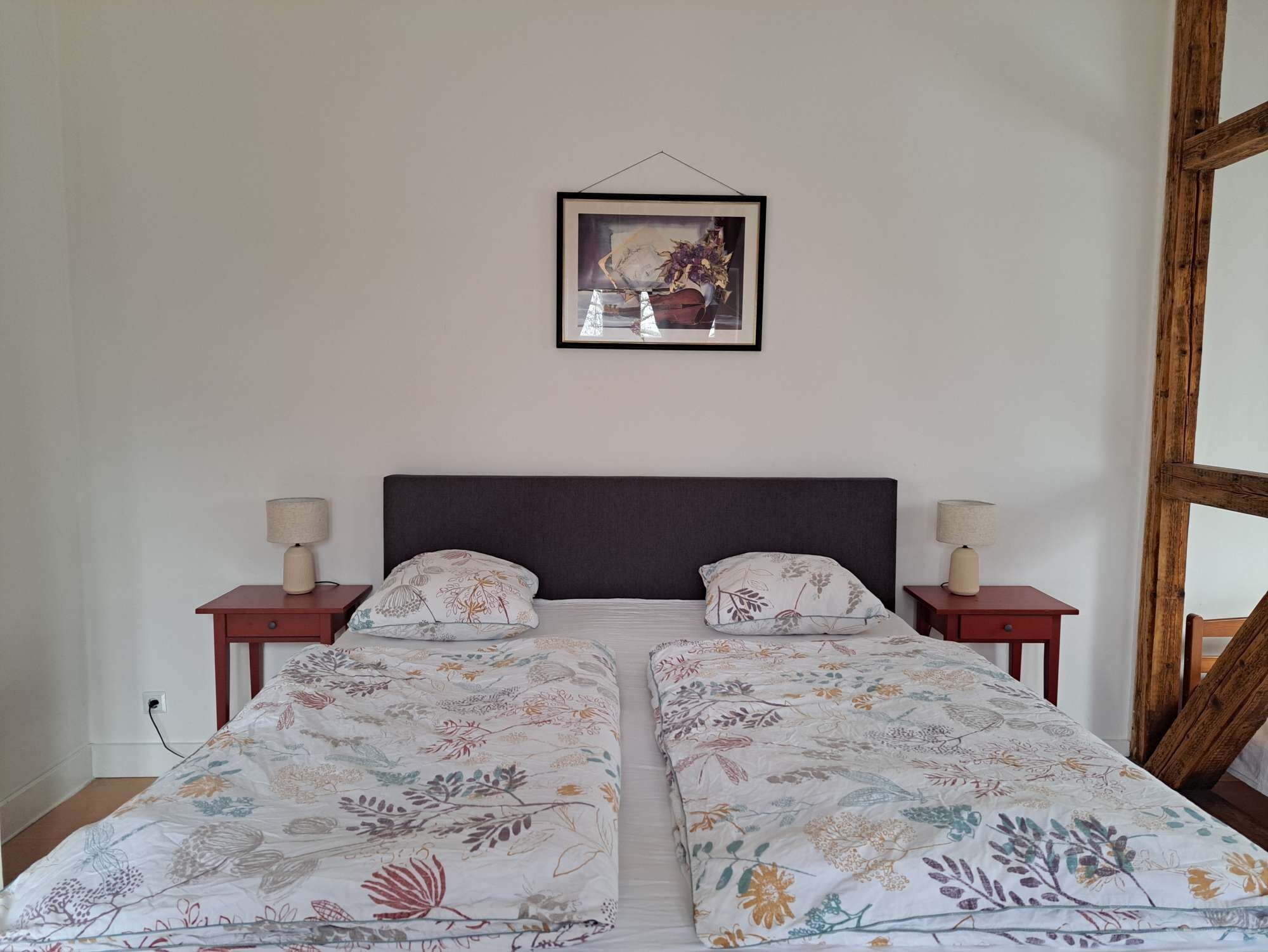 Ein Doppelbett mit floraler Bettwäsche, zwei Nachttische mit Lampen, ein Holz-Kopfteil und ein gerahmtes Bild an der Wand.