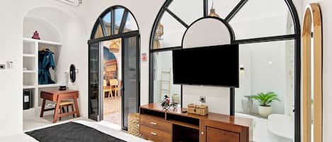 A hotel room with a large arched window, a flat-screen TV, a wooden console table, and a black patterned rug.