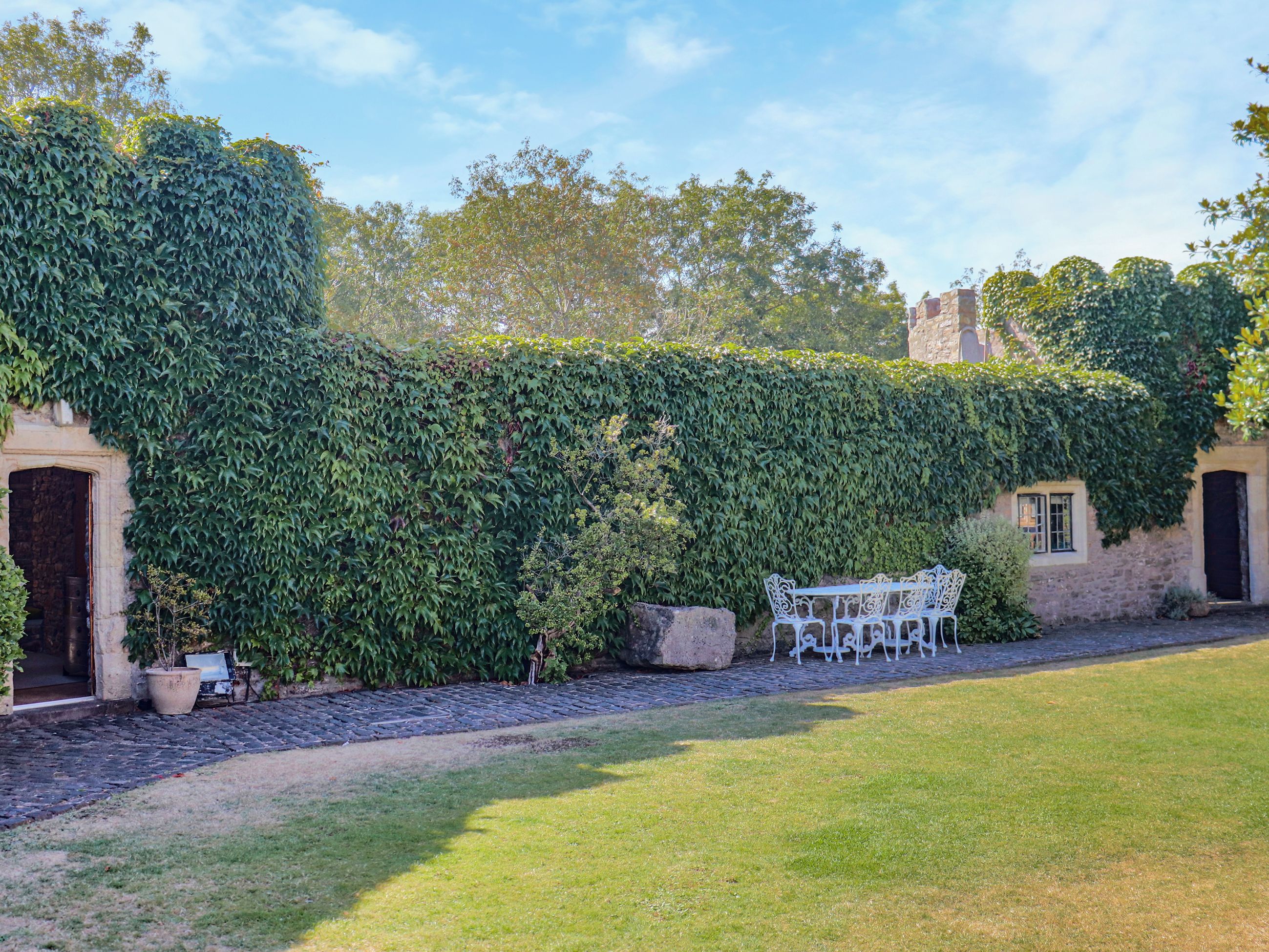 A stone building partially covered by ivy, a white metal bench, and a paved pathway.