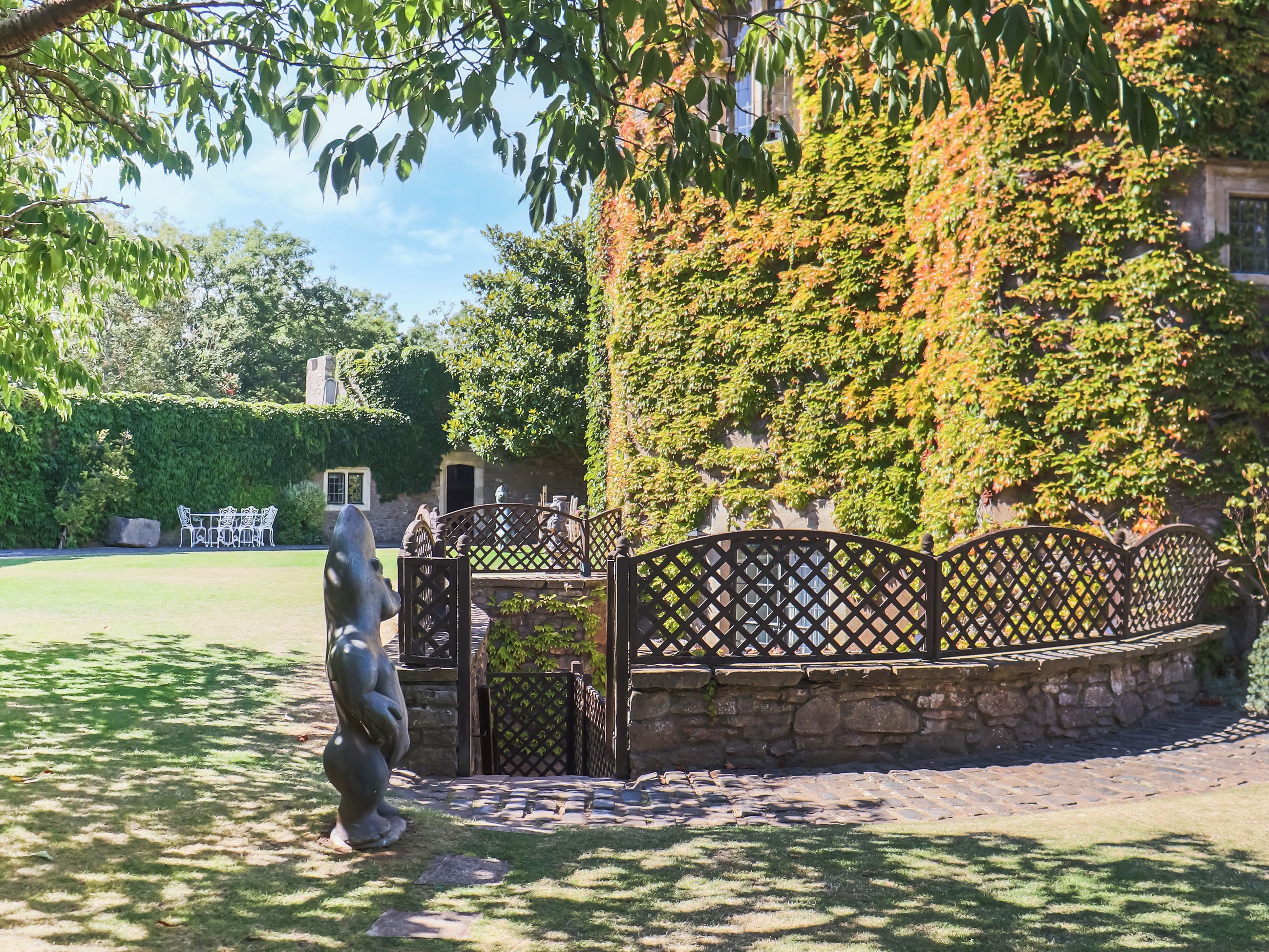 Ein Garten mit Steinmauer, Metallzaun und einer Statue.