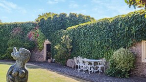 A garden with a stone wall, a white metal bench, and a sculpture. - 7 bedroom accommodation in Clevedon (Clevedon)