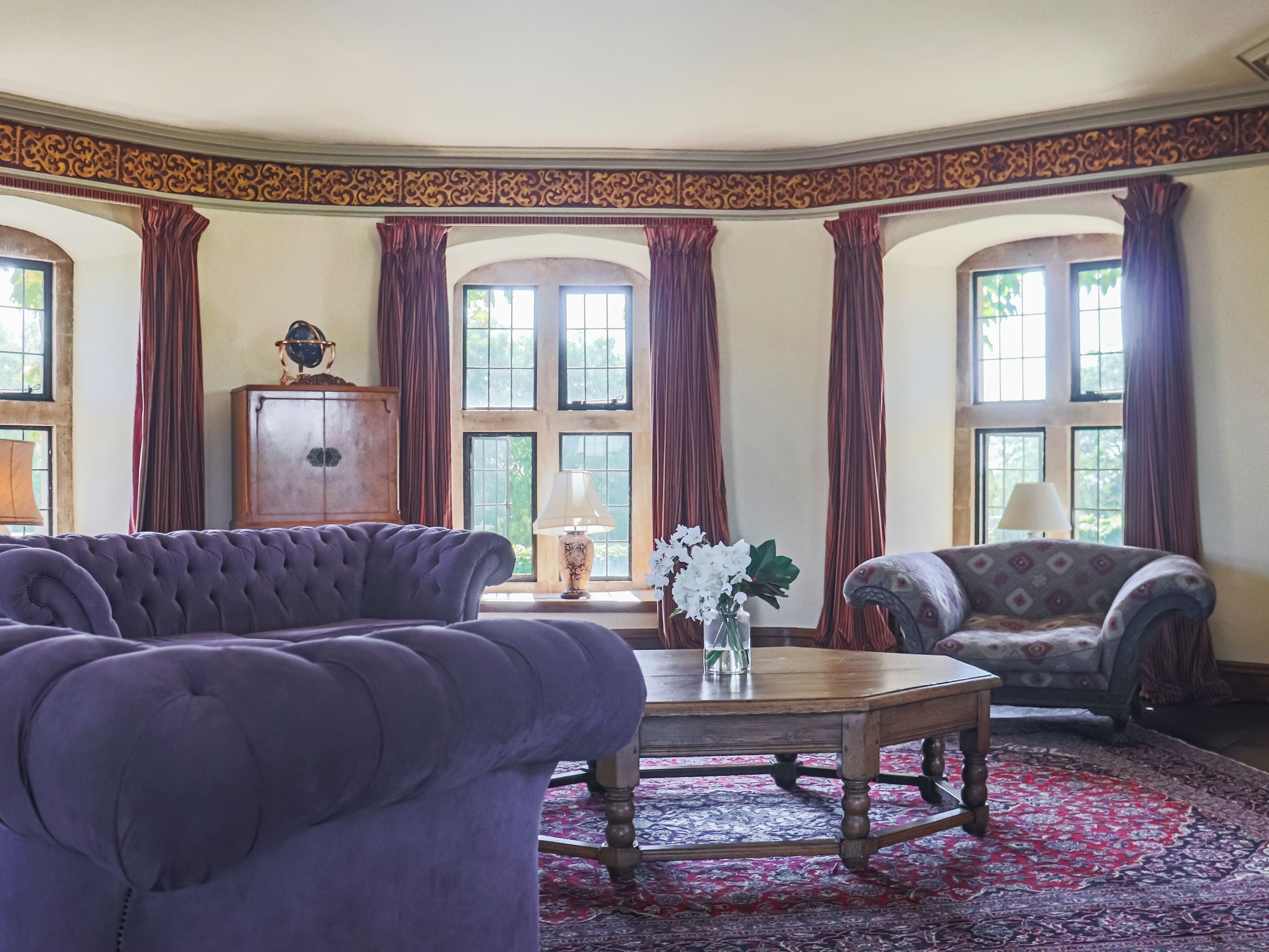 Une pièce avec un canapé violet, une table basse en bois et deux fauteuils. Un tapis à motifs recouvre le sol, et on peut apercevoir un meuble dont le dessus est décoratif.