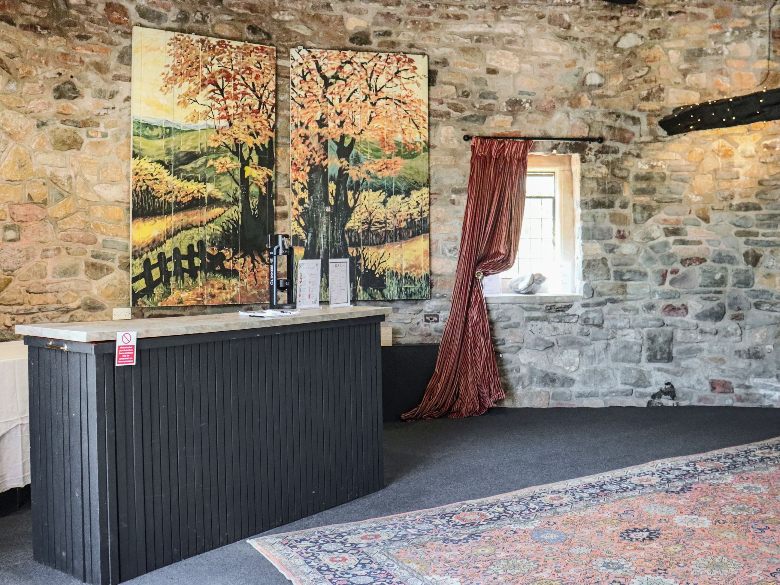 Ein Zimmer mit Steinwänden, einer Bar, einem gemusterten Teppich und einem Fenster mit Vorhang.