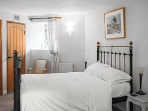 Un dormitorio con cama, una silla, un radiador, un cuadro en la pared y una puerta.