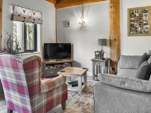 Ein Wohnzimmer mit Fernseher, einem karierten Sessel, einem grauen Sofa, einem Holztisch und einer wandmontierten Leuchte.