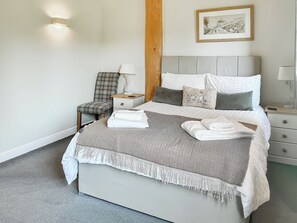 Ein ordentlich bezogenes Bett mit einer grau-weißen Zickzack-Decke, einem Kissen mit Blumenmuster und einem Nachttisch mit Lampe.