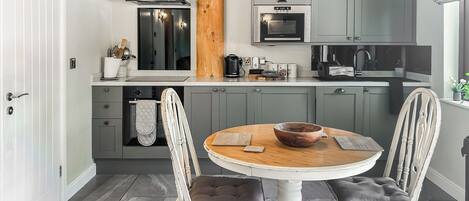 Una cocina moderna con armarios grises, un horno empotrado y una mesa redonda de madera con dos sillas.