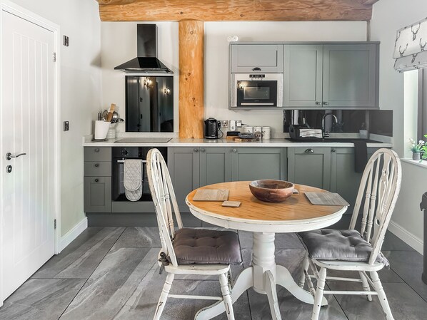 Eine moderne Küche mit grauen Schränken, einem eingebauten Backofen und einem runden Holztisch mit zwei Stühlen.
