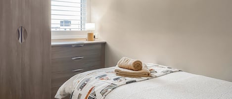 Ein Schlafzimmer mit einem Bett, einem Nachttisch mit Lampe, einem Kleiderschrank und einem Fenster mit Jalousien.