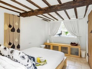 A bedroom with a bed, a window with curtains, a wooden cabinet, and a small window with a view of the outside. - 3 bedroom accommodation in Southrop (Southrop)