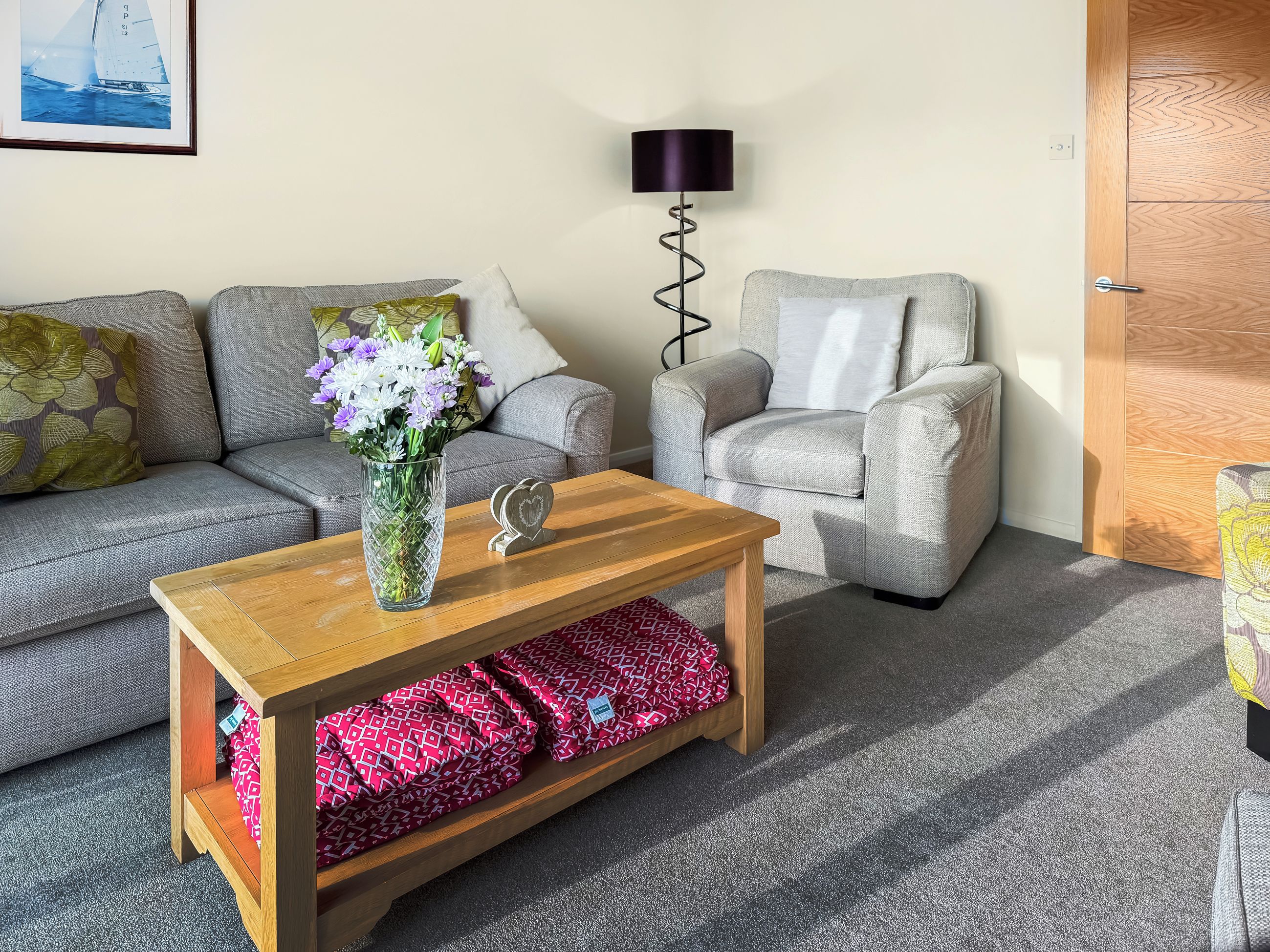 Un salon avec un canapé gris, un fauteuil gris, une table basse en bois et un vase rempli de fleurs.