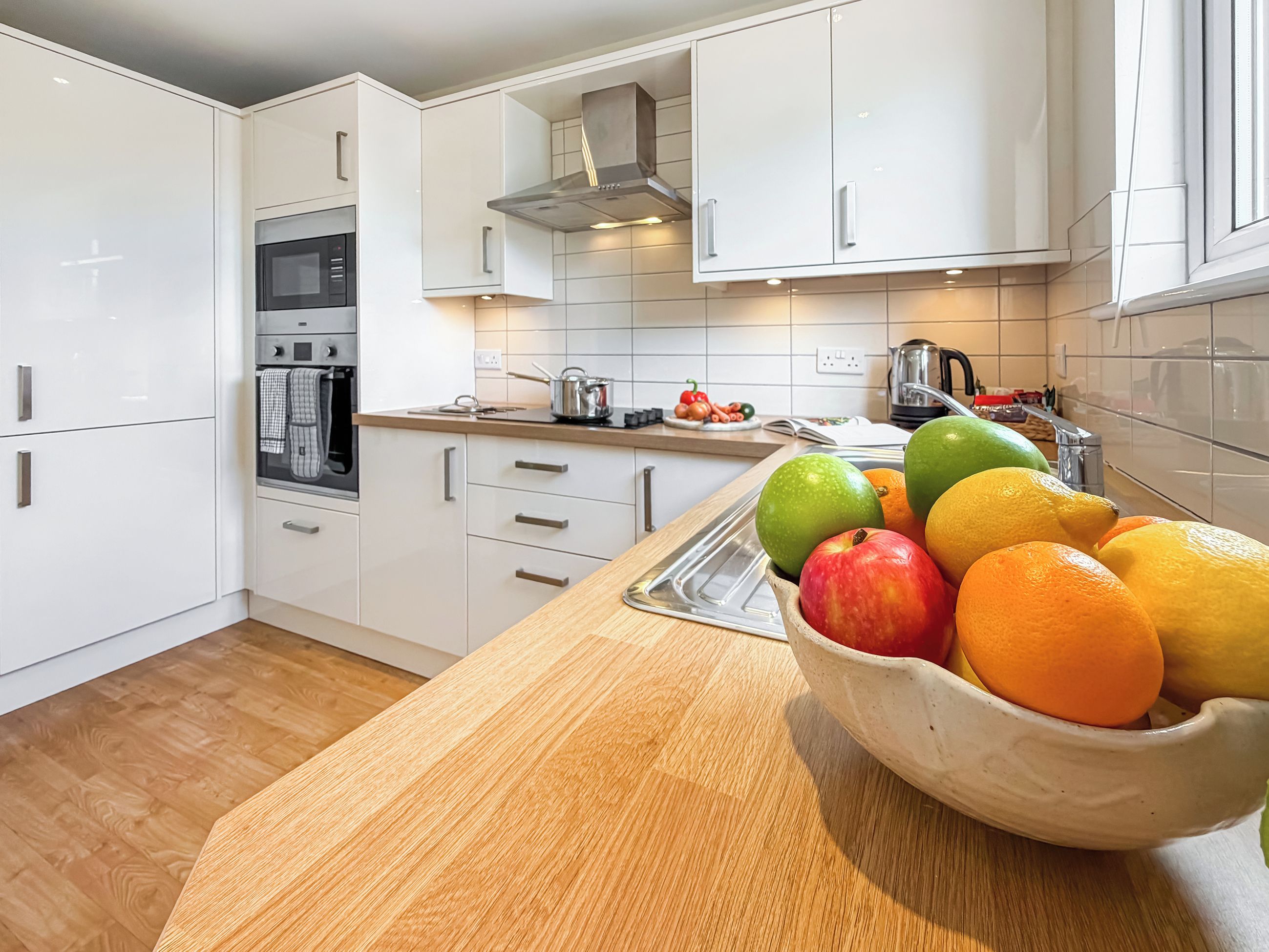 Eine moderne Küche mit weißen Schränken, einer Holz Arbeitsplatte und einer Schüssel mit Obst.