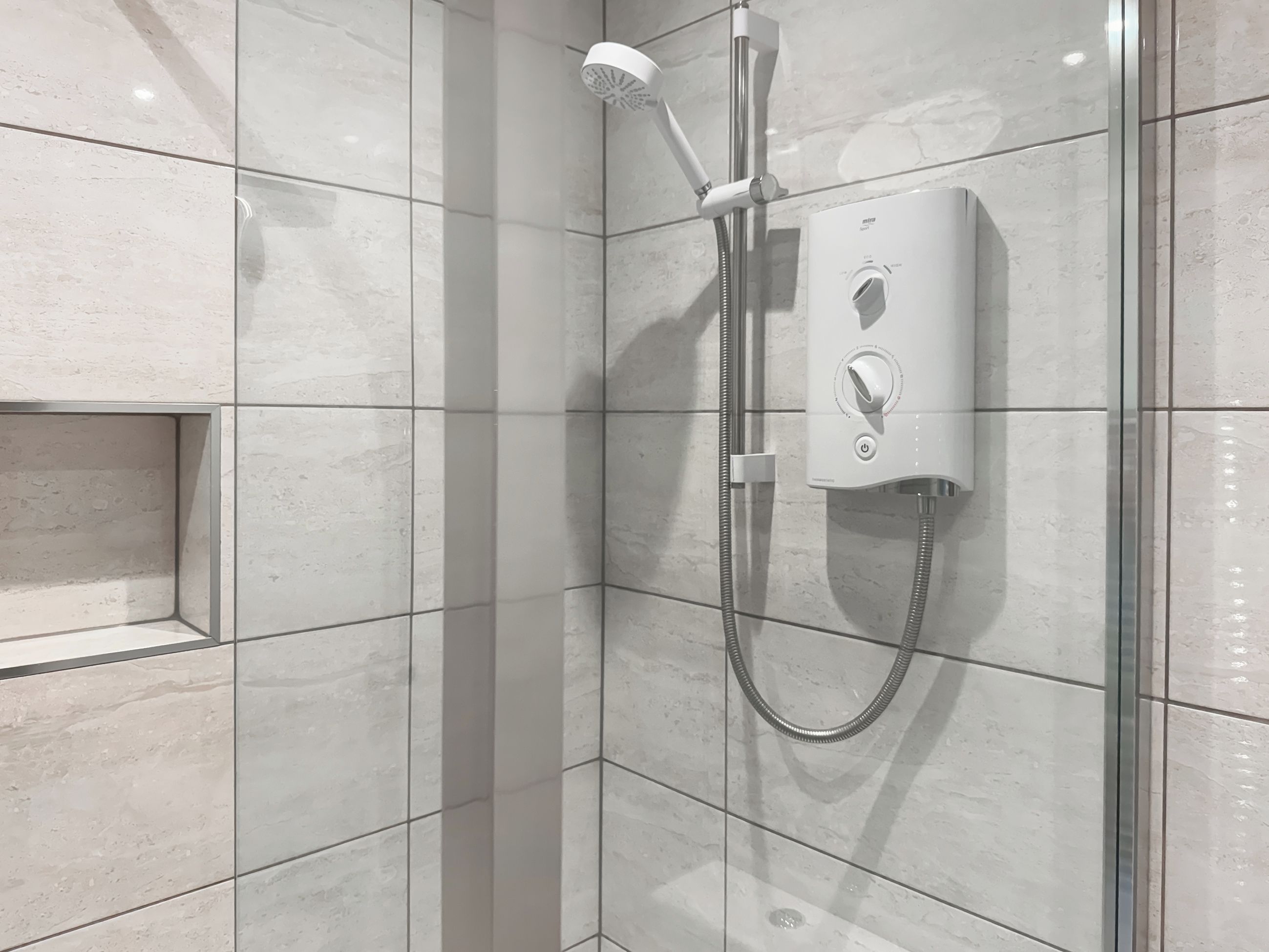 Une douche équipée d’un pommeau de douche à main et d  ’un panneau de commande fixé au mur.