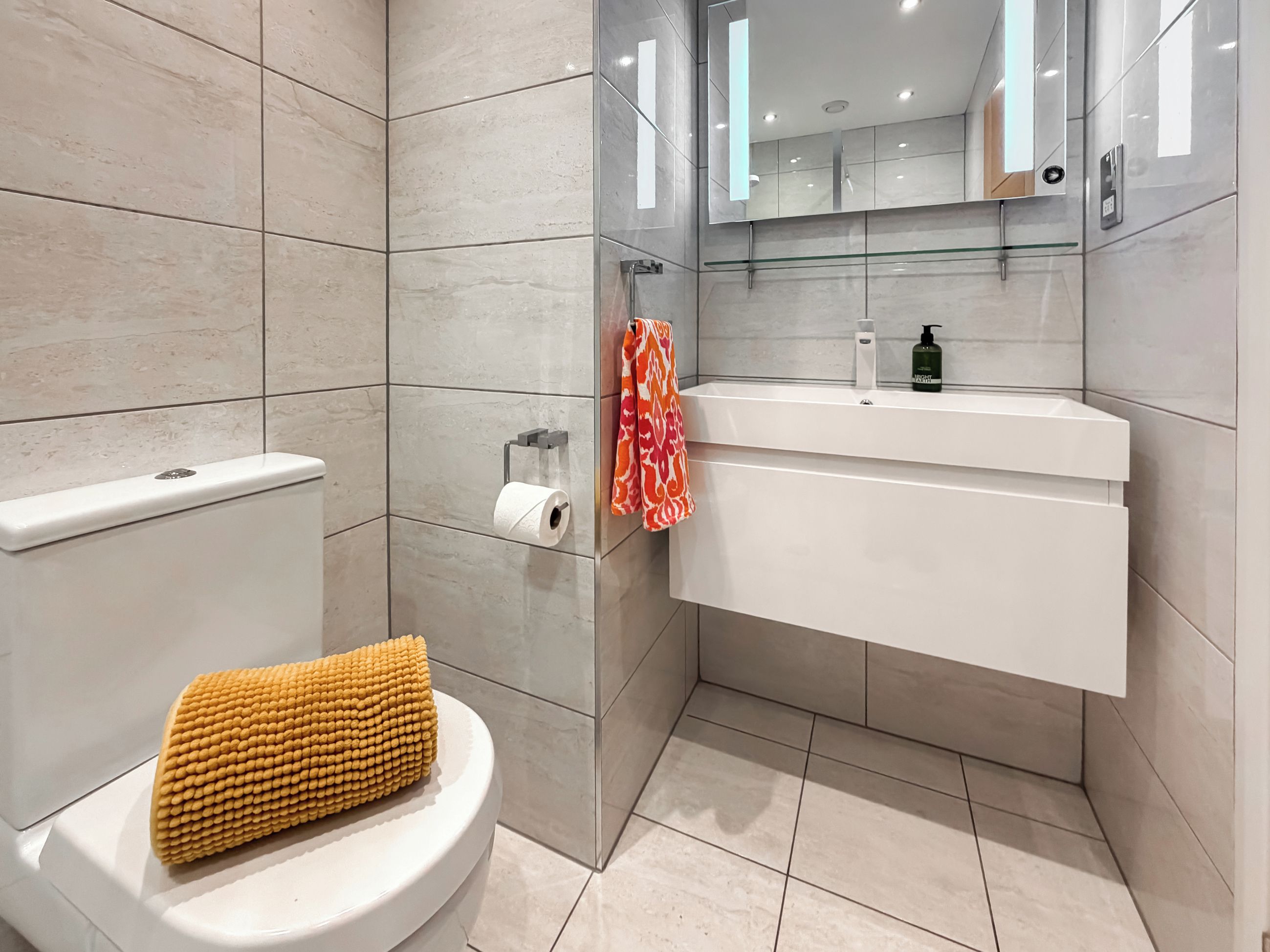 Une salle de bain moderne comprenant des toilettes, une douche à parois de verre, un lavabo avec un miroir et un porte-serviettes.