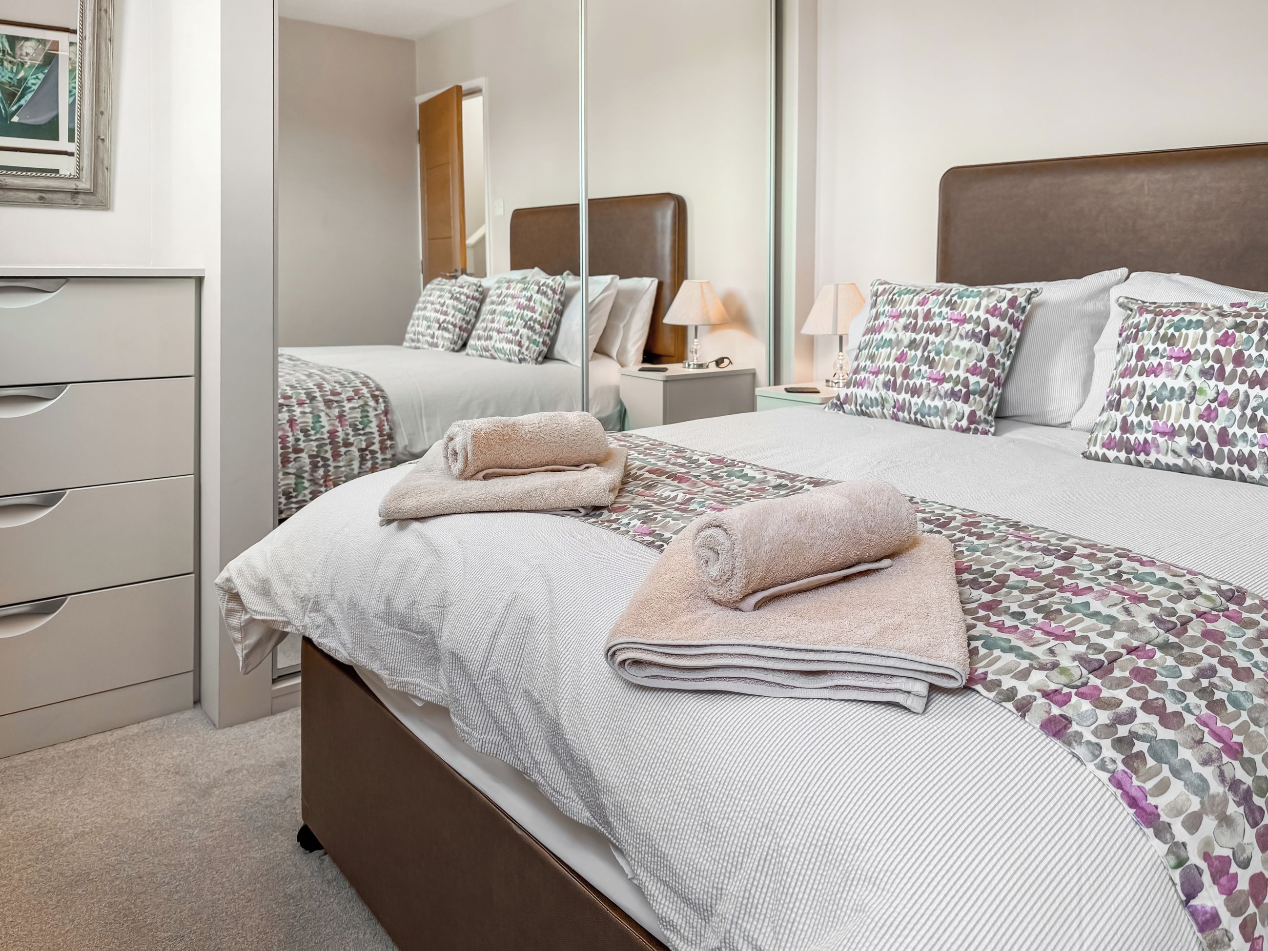 Une chambre d’hôtel comprenant un lit, une commode, un miroir et une table de chevet avec une lampe.