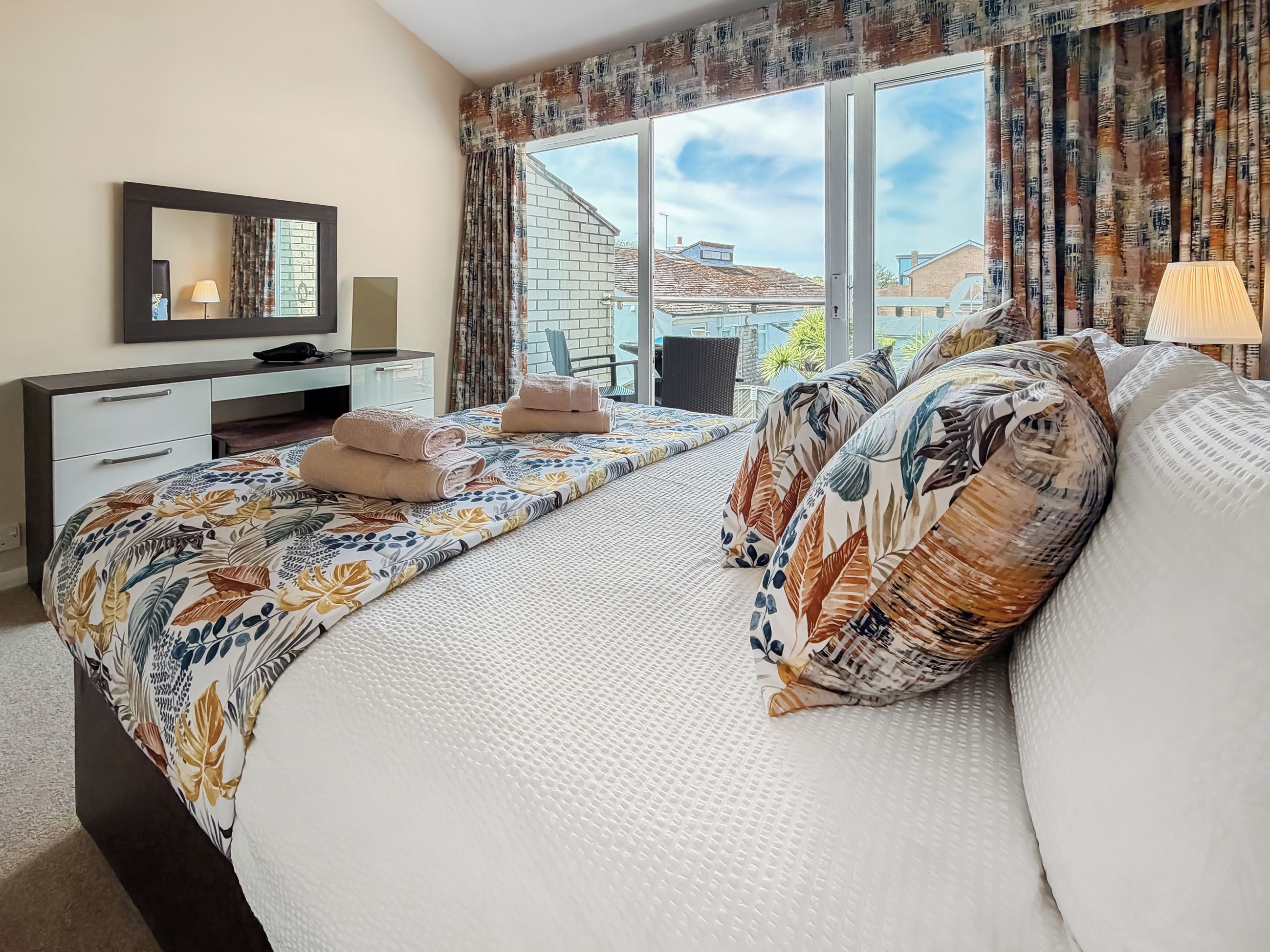 Een hotelkamer met een bed, een bureau, een stoel en een raam met uitzicht op gebouwen.
