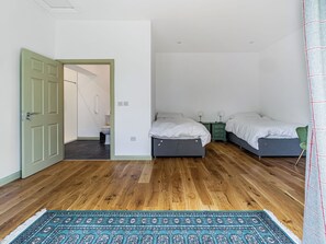A bedroom with two beds, a wooden floor, a patterned rug, and a green door. - Ultimate Country House (Boston)