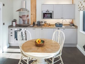 A modern kitchen with white cabinetry, a microwave, a stove, and a dining area with a round table and chairs. - Knotty and Nice - UKC9953 (Harrogate)