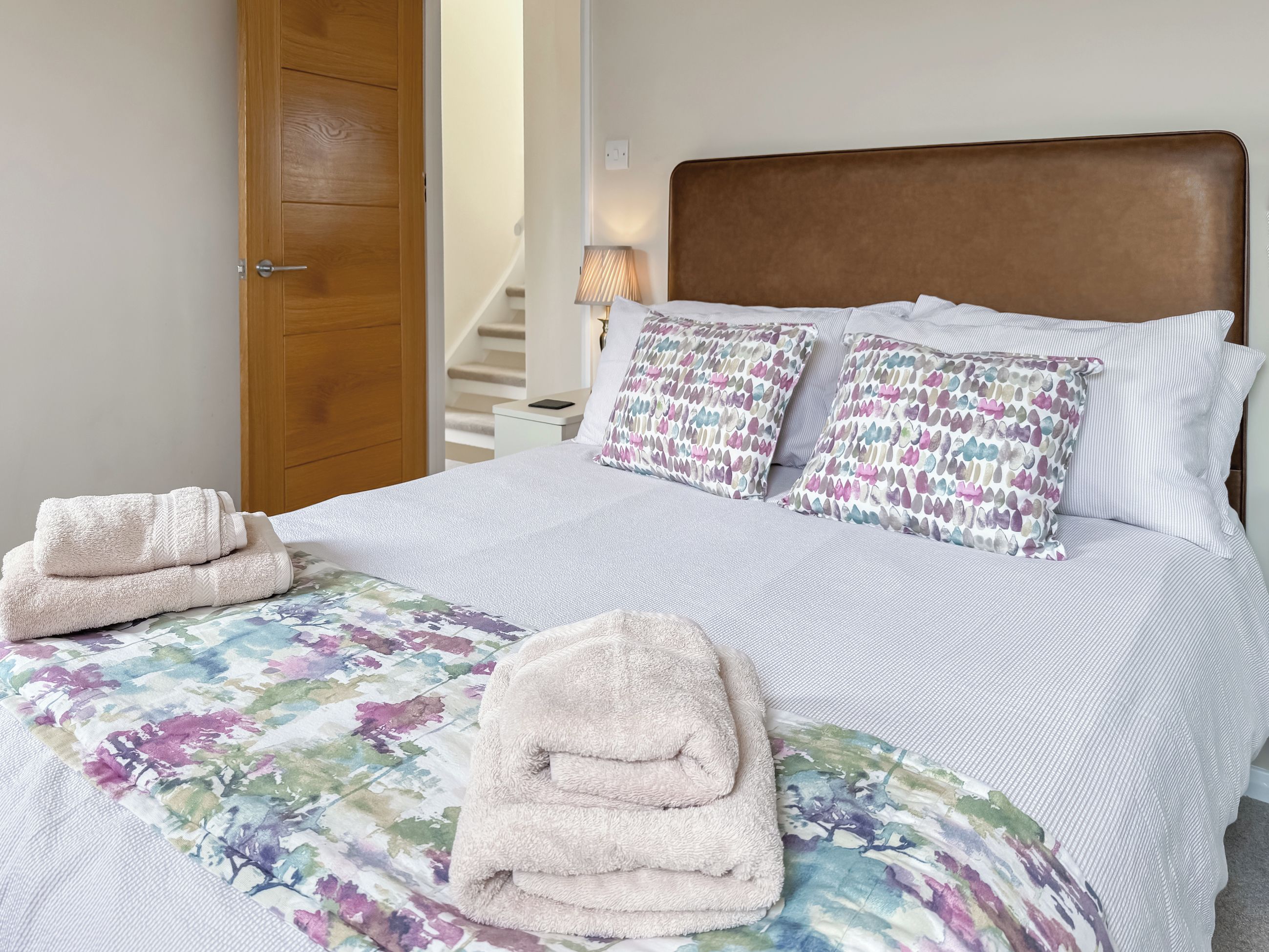 A neatly made bed with a floral-patterned bedspread, two patterned pillows, and two folded towels on the side.