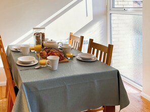 Ein Frühstückstisch gedeckt mit Tellern, Tassen, einer Teekanne, einem Croissant und einem Glas Orangensaft.