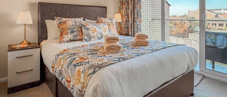A hotel room with a large bed, two bedside tables, a window with a view of buildings, and a balcony.