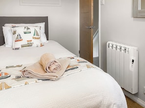 A neatly made bed with a patterned duvet, a rolled towel, and a pillow with a nautical theme. - 3 bedroom accommodation in Christchurch (Christchurch)