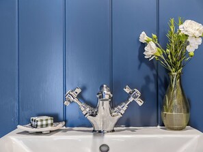 A bathroom sink with a chrome faucet, a white vase with white flowers, and a checkered soap dish. - Da Vincis Den - UKC9977 (North Tawton)