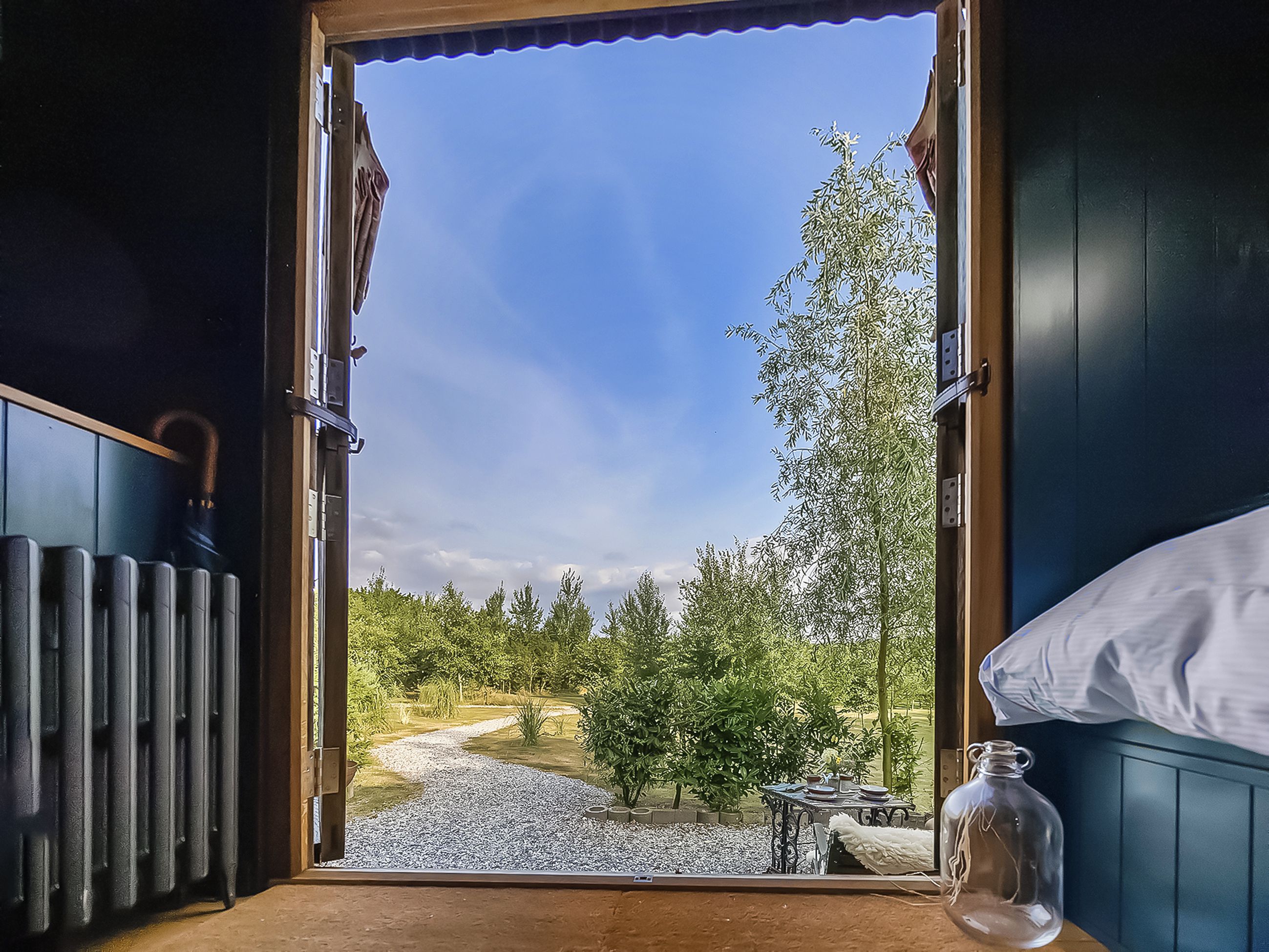 A room with a view of a garden, a table with dishes, and a bottle on the windowsill.