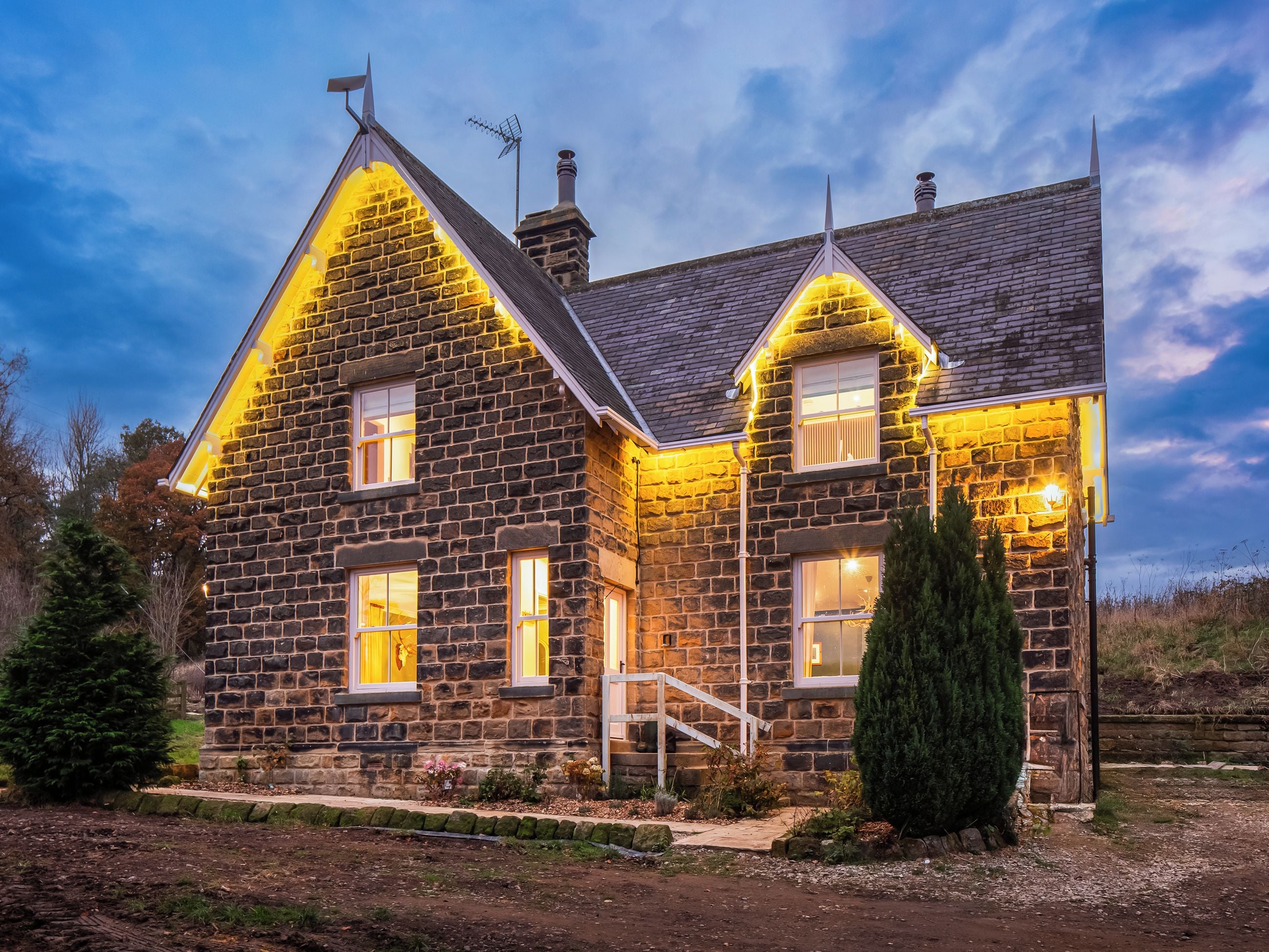Une maison en pierre avec un toit à pignon abrupt, une cheminée et un petit porche avec des marches menant à l’entrée.