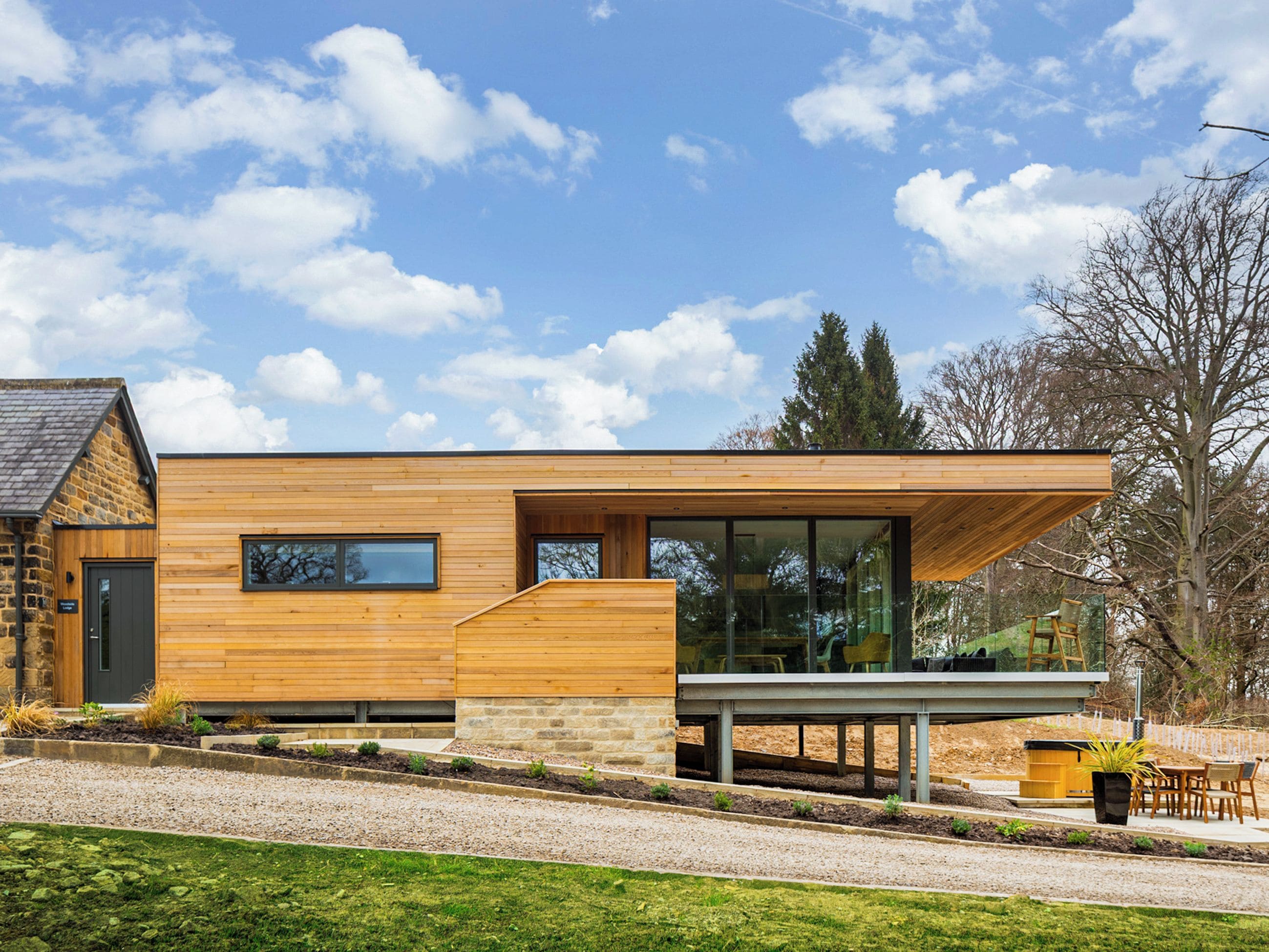 Une maison moderne à deux étages, dotée d’une façade en bois, de grandes fenêtres et de fondations en pierre.