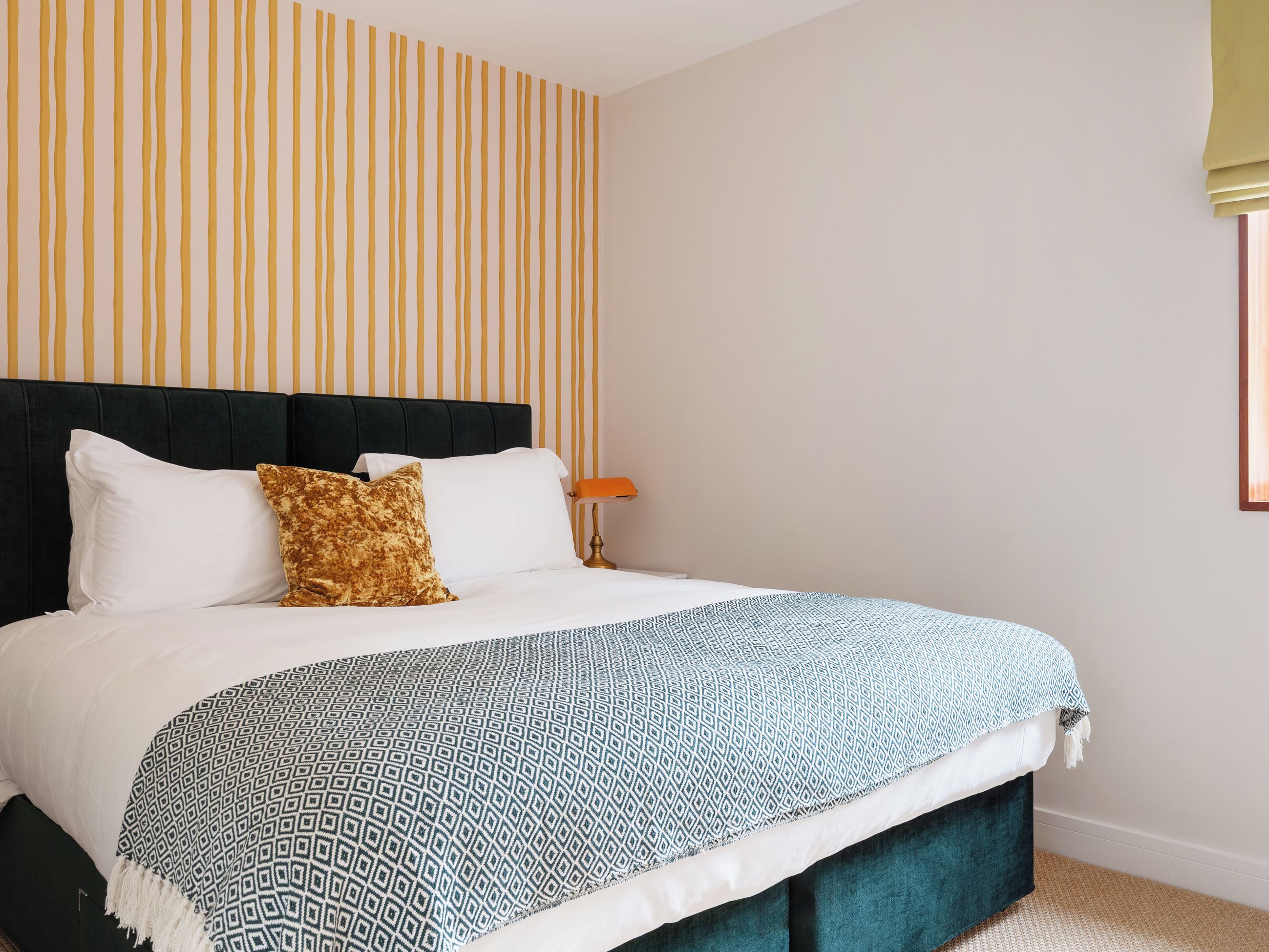 A bed with a dark headboard, white and patterned bedding, and a striped wall behind.